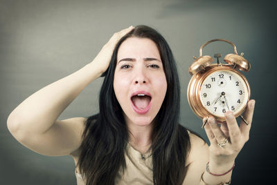 Portrait of woman screaming while holding alarm clock against gray background