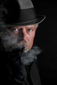 Close-up portrait of senior man smoking against black background
