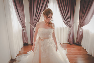 Beautiful woman in wedding dress looking away while standing at home