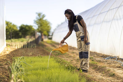 Female farmer watering plants while standing at organic farm