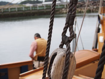 Close-up of rope tied on boat with man sitting in background