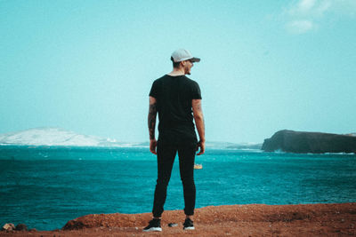 Rear view of man standing at beach against sky