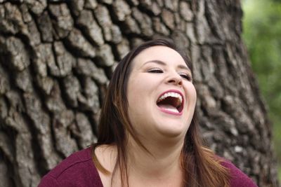 Close-up of young woman looking away while laughing against tree trunk