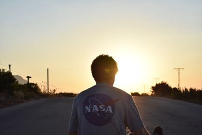 Rear view of man standing on road against sky during sunset