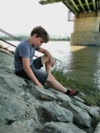 Boy sitting on stones at riverbank