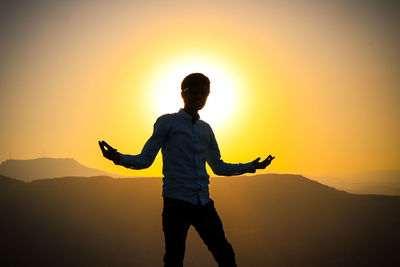 Man with arms outstretched standing against sky during sunset