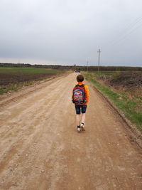 Rear view of boy walking on dirt road against sky