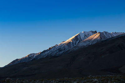 Low angle view of snowcapped mountain against clear blue sky