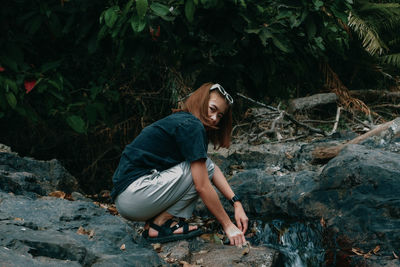 Young woman looking away while sitting on rock in forest