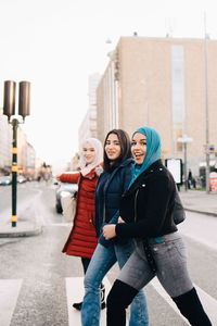 Side view of portrait of smiling female friends crossing street in city