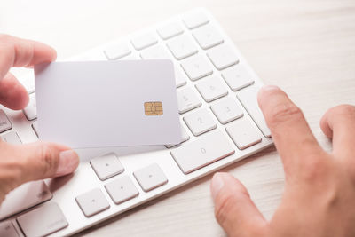 Cropped hand of person holding credit card while using computer keyboard