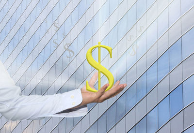 Digital composite image of man holding dollar sign against building with shadows