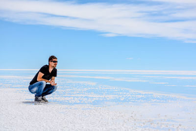 Full length of man crouching on dessert against sky