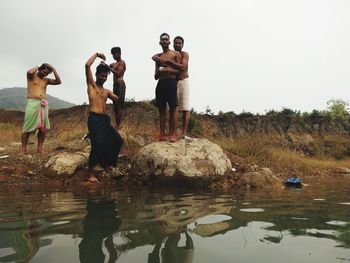 People standing on rock by lake against sky