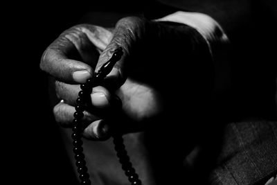 Cropped hand of man holding rosary beads while praying