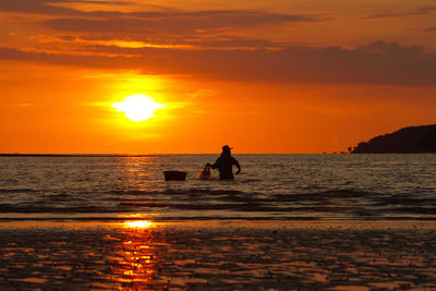 Silhouette man standing on shore against orange sunset sky