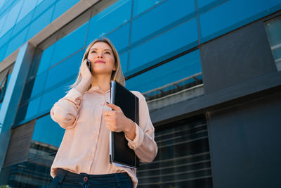 Low angle view of young woman standing against building in city