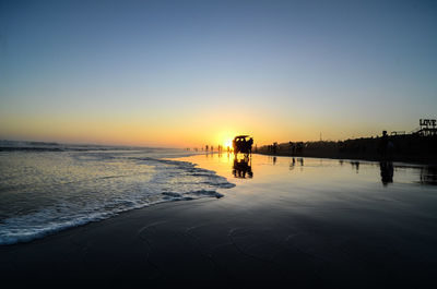 Silhouette people on beach against clear sky during sunset