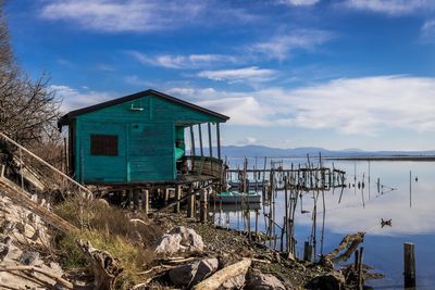 Stilt house by lake against sky