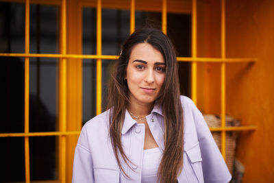 Portrait of smiling young woman standing against window