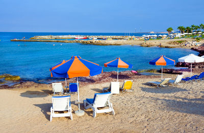 Lounge chairs and parasols on beach against sky