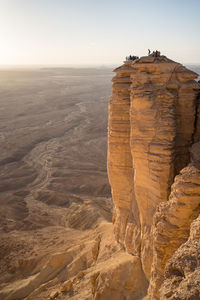From above group of anonymous travelers contemplating colorful sundown while visiting the edge of the world in saudi arabia
