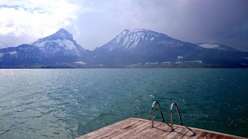 Ladder on jetty over river by mountain against cloudy sky