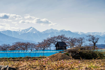 Built structure on field by snowcapped mountains against sky