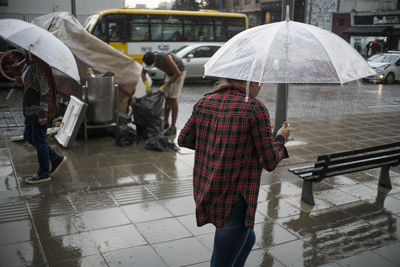 Rear view of mid adult woman with umbrella walking on street during rainfall