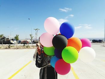 Woman holding multi colored balloons against sky in city
