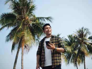 Low angle view of young man using smart phone against sky