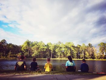 Rear view of people sitting by lake against sky