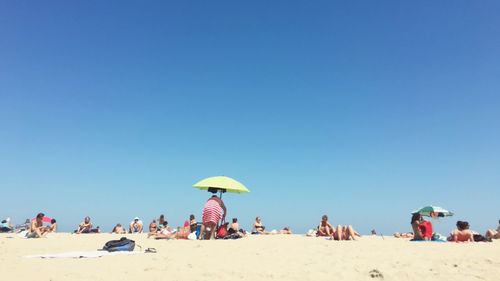 People at beach against clear blue sky