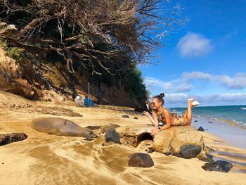 People sitting on rock by sea against sky