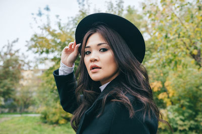 Portrait of beautiful young woman standing against trees