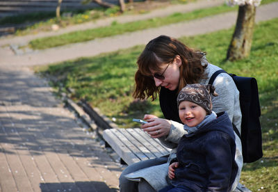 Portrait of son with mother text messaging on bench in park