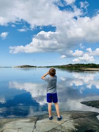 Rear view of boy standing by lake against sky