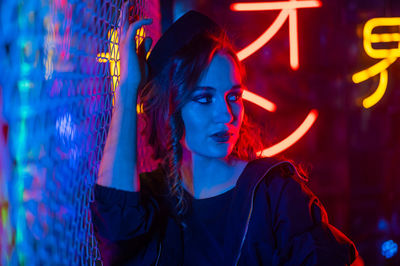 Portrait of young woman standing against illuminated lighting equipment