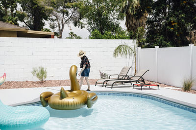 Woman wearing hat cleaning swimming pool with pole during vacation