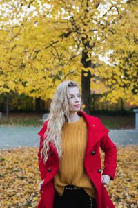 Young woman looking away while standing at park during autumn