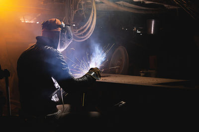 Welder in a workshop welds a metal part. general plan of an old cluttered garage where a man in