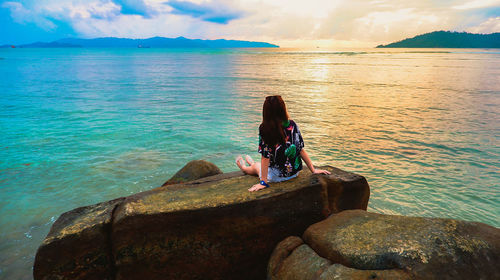 Man sitting on rock by sea against sky