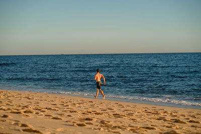 Full length of man running on beach against clear sky