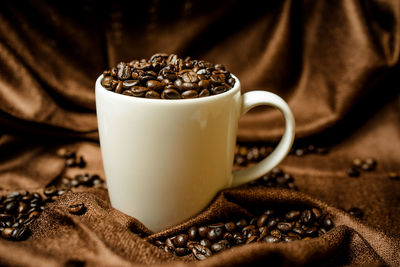 Close-up of roasted coffee beans with cup on fabric