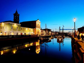 Illuminated bridge over dock by buildings against sky at dusk