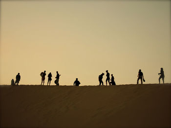 Silhouette people at desert against clear sky during sunset