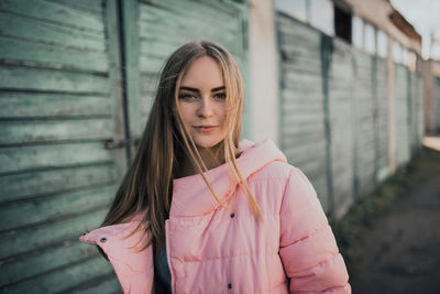 Young gorgeous blonde girl dressed fashion pink jacket and blue jeans. old azure cerulean fence