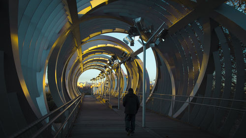 Rear view of man walking on footbridge in tunnel