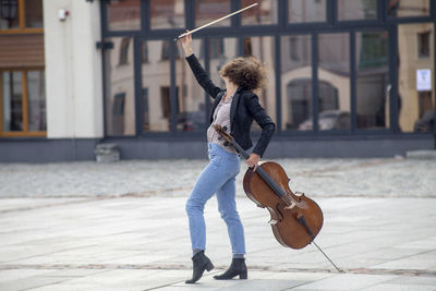 Smiling woman holding violin while dancing on street