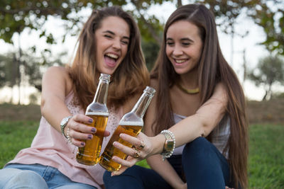 Happy friends enjoying beer while sitting on grass at park